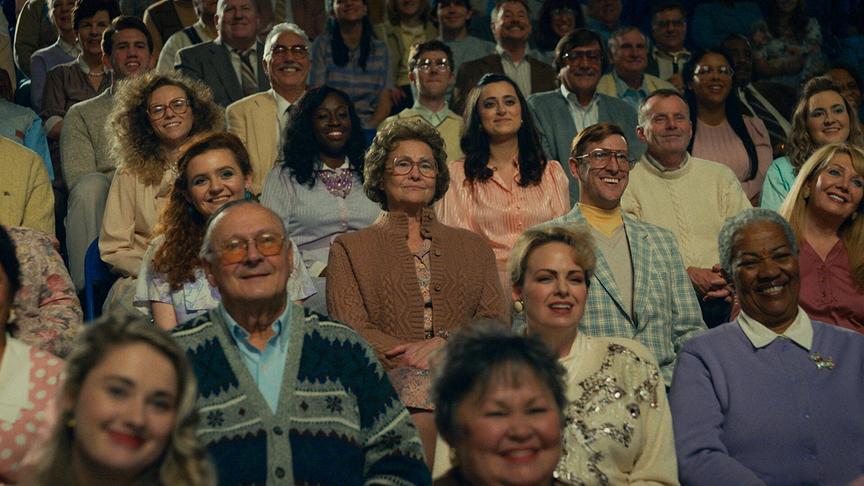 Das Publikum auf der Tribüne blickt fröhlich lächelnd.