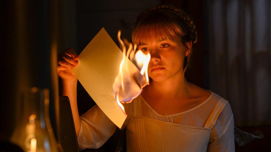 Ein Mädchen hält ein brennendes Blatt Papier in der Hand und beobachtet es.