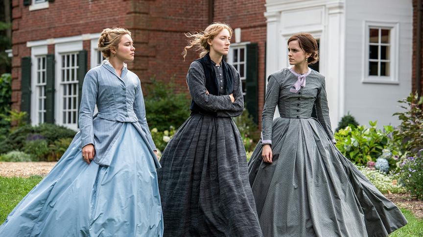 Drei Mädchen in wehenden Kleidern gehen ernst blickend nebeneinander.