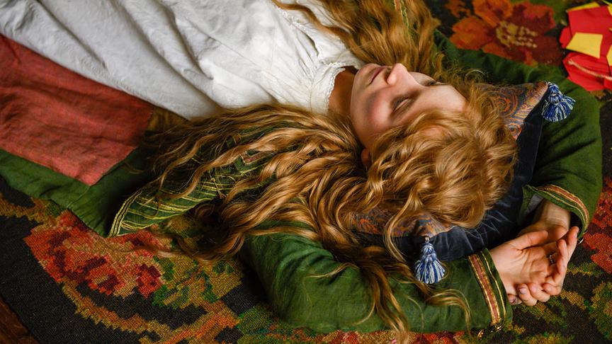 Ein Mädchen liegt mit Armen über dem Kopf verschränkt flach auf dem Boden, ihre Locken fallen offen um sie herum.