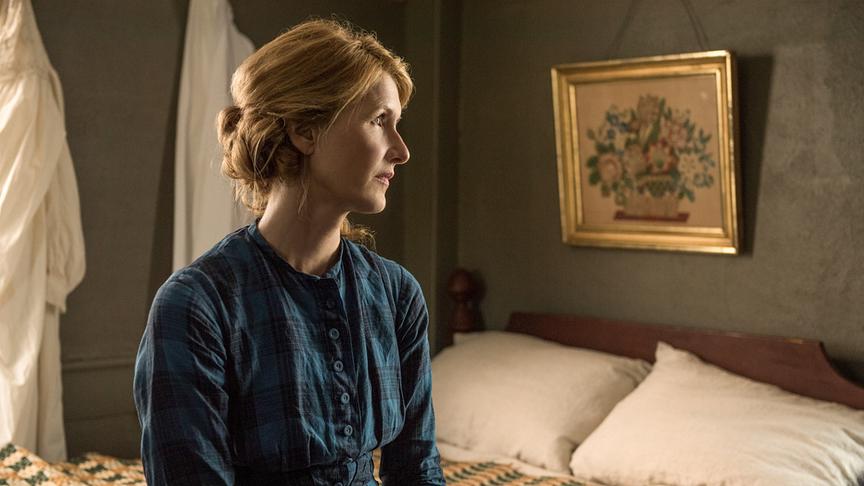 Frau sitzt auf einem Bett und blickt in die Ferne.