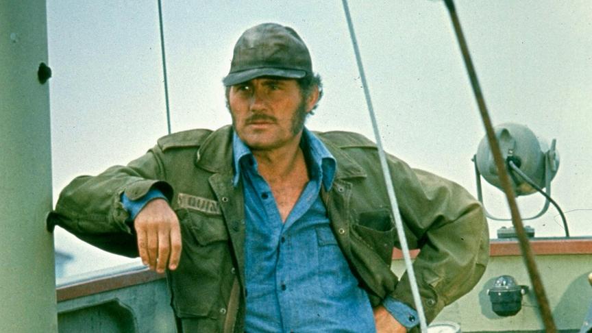 Mann mit Kappe lehnt sich an Schiffsmast