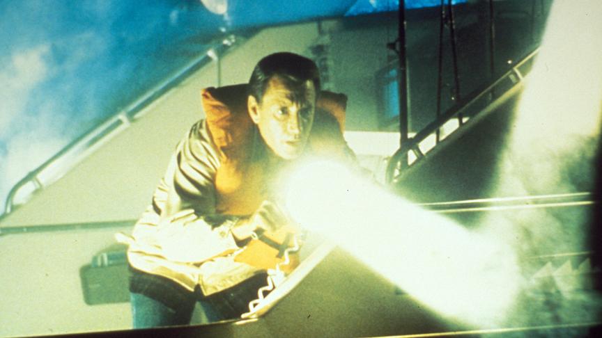 Mann mit Schwimmweste nutzt einen Scheinwerfer um vom Boot aus hinabzuleuchten