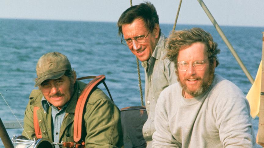 Drei Männer auf einem Boot, eine Angel hängt vor ihnen ins Wasser