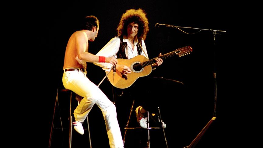 Freddie Mercury halb sitzend und Brian May an der Gitarre auf der Bühne.