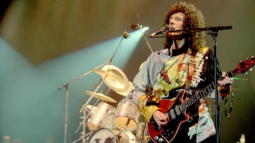 Brian May an der Gitarre und am Mikrofon auf einer Bühne.