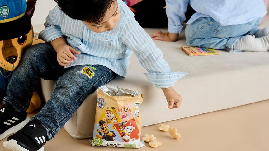 Ein kleiner Bub nimmt Knabbergebäck von PURE&FUN aus der Tüte.