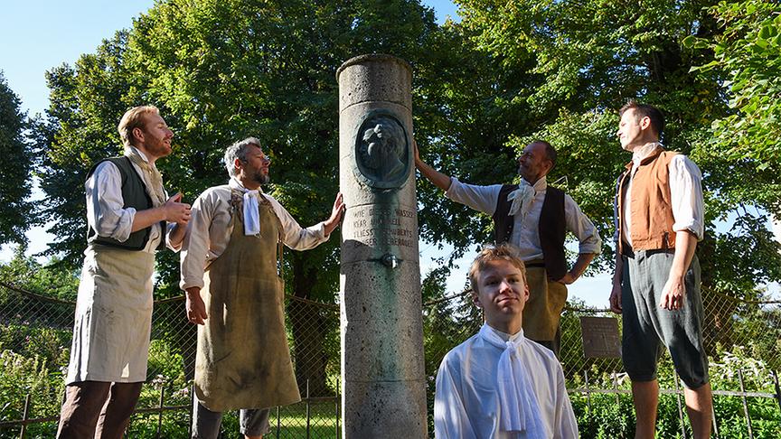 Eine Acapella-Gruppe (Florian Sebastian Fitz, Gerald Huber, Terry Chladt und Stefan Bleiberschnig) singt „Am Brunnen vor dem Tore“ vor der Ochsenburg.