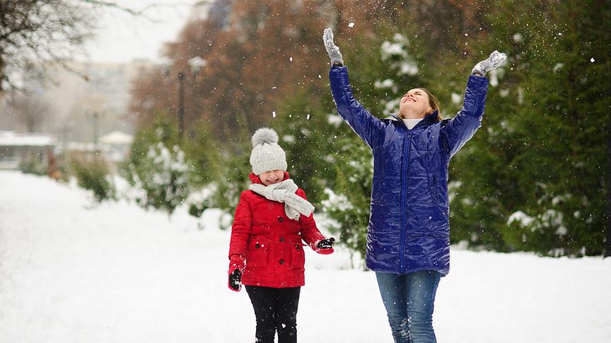 Mutter mit Kind freut sich über Schnee.