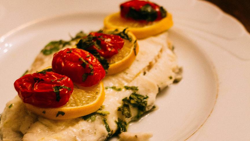 © Unsplash (Beispielfoto) Fischfilet mit Zitronenscheiben und gedünsteten Tomaten