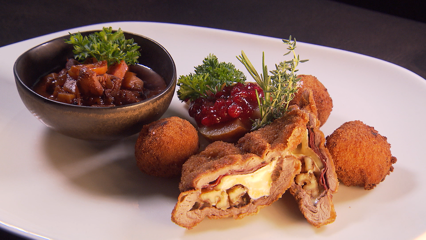 © ORF Reh-Cordon-Bleu mit knuspriger Panade, Rehragout, goldbraunen Kürbisrisotto-Pralinen und Preiselbeerbirne auf einem Teller angerichtet.