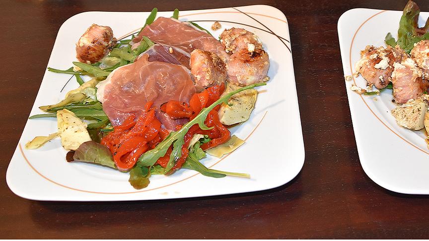 ZIEGENKÄSE MIT PROSCIUTTO AUF RUCCOLA-SALAT: Ziegenkäse in Hamburger Speck einwickeln, abbraten, auf Ruccola-Salat mit Prosciutto und gegrillten Paprika und Artischocken anrichten.