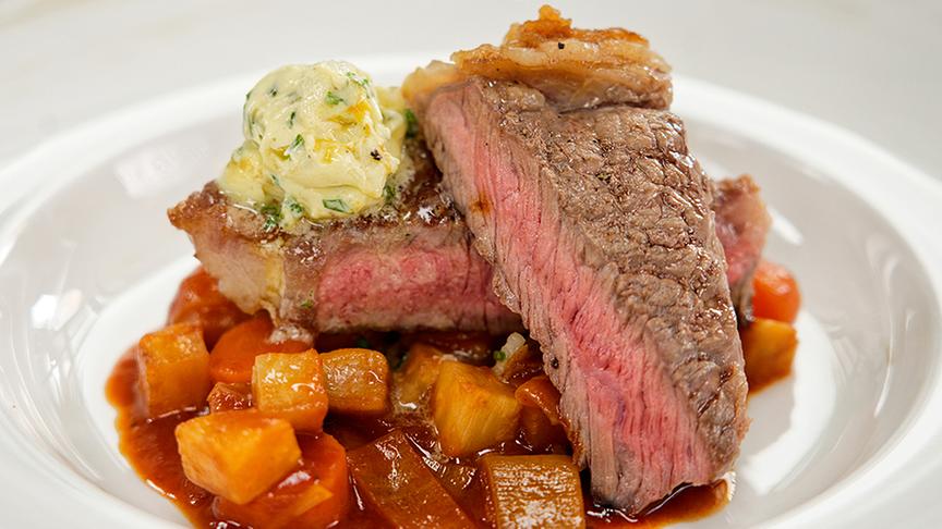 Rosa gebratenes Rinderrücken-Steak mit Schmorgemüse und Kräuterbutter