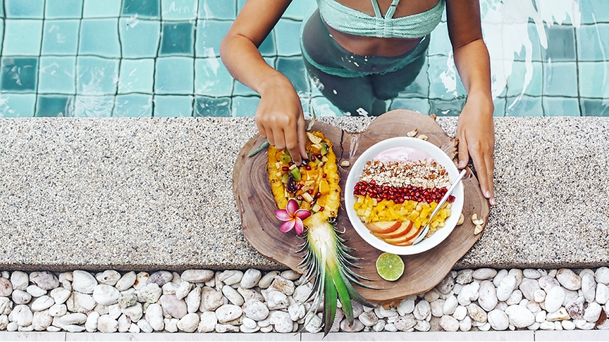 Eine Frau im Pool nascht frisches Obst