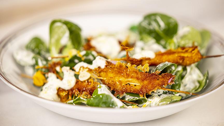 Schnelle Kartoffel Würfel und Knusprige Hühnerspieße auf Blattsalat mit Kräutersauce angerichtet auf einem Teller