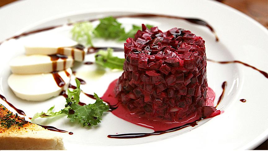 Rotes Rüben Tartare angerichtet in Zylinderform auf einem Teller mit Beilagen