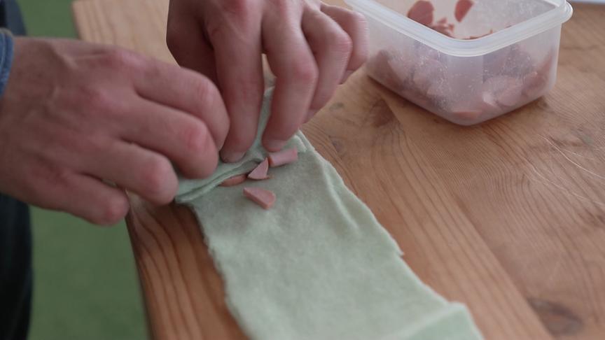 Ein Mann rollt Wurststückchen in Stoff ein