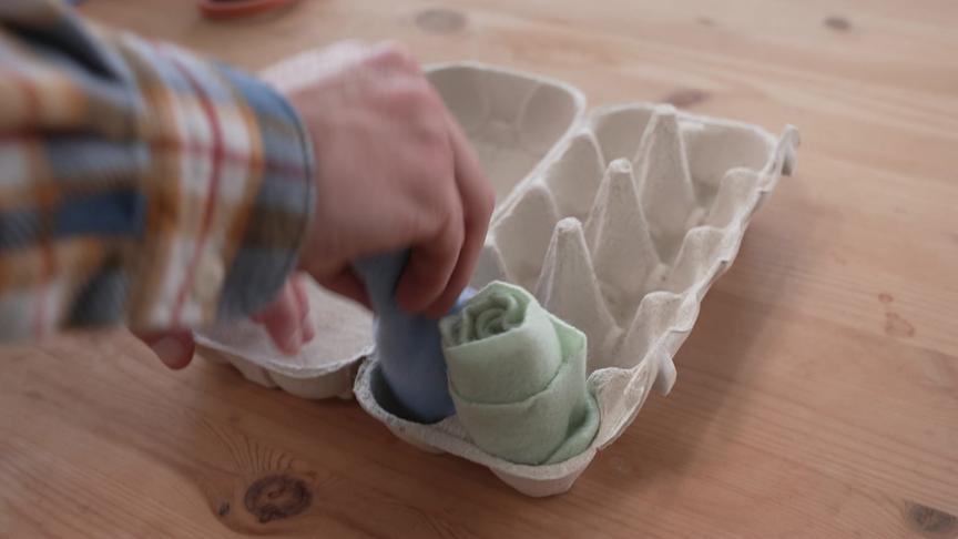 Ein Mann steckt gerollte Stoffe aufrecht in einen Eierkarton