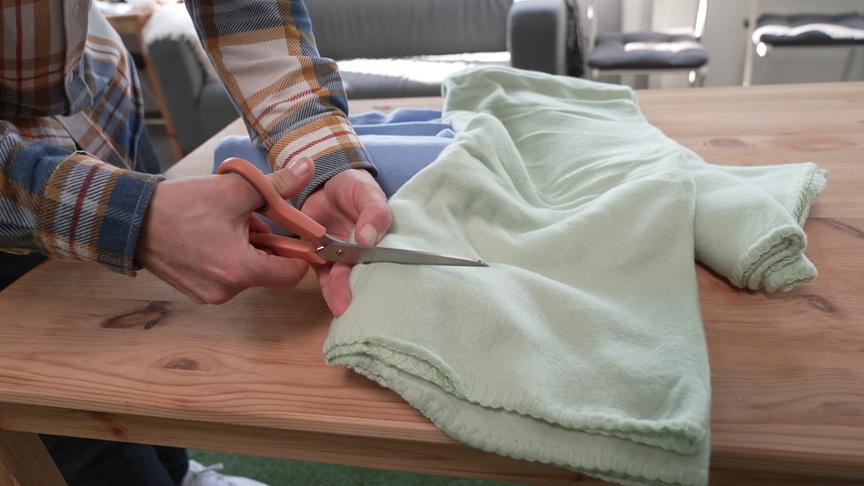 Mann schneidet mit Schere eine Decke in Streifen