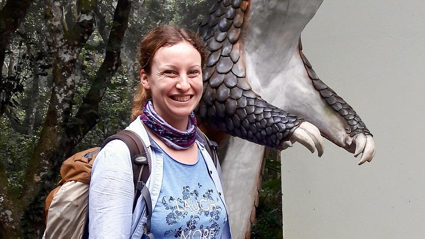 Eine Frau steht vor einer Gürteltier-Statue und lacht in die Kamera.