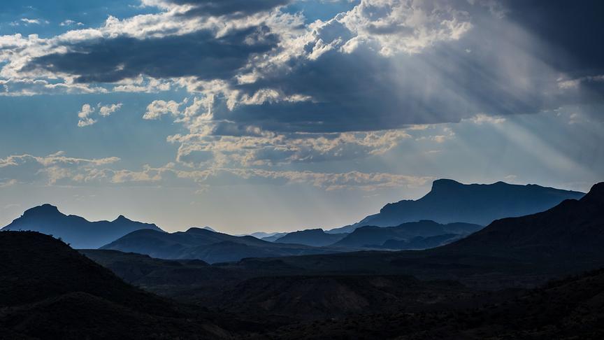 Bergige Landschaft bei schönem Wetter. Die Sonne strahlt sichtbar durch die Wolken hindurch.