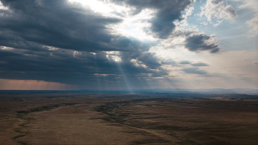 © Foto: ORF/LE CINQUIEME REVE Dunkle Wolkenstimmung mit vereinzelt Sonnenstrahlen, die durch die Wolkendecke brechen über einer kargen, flachen Ebene.