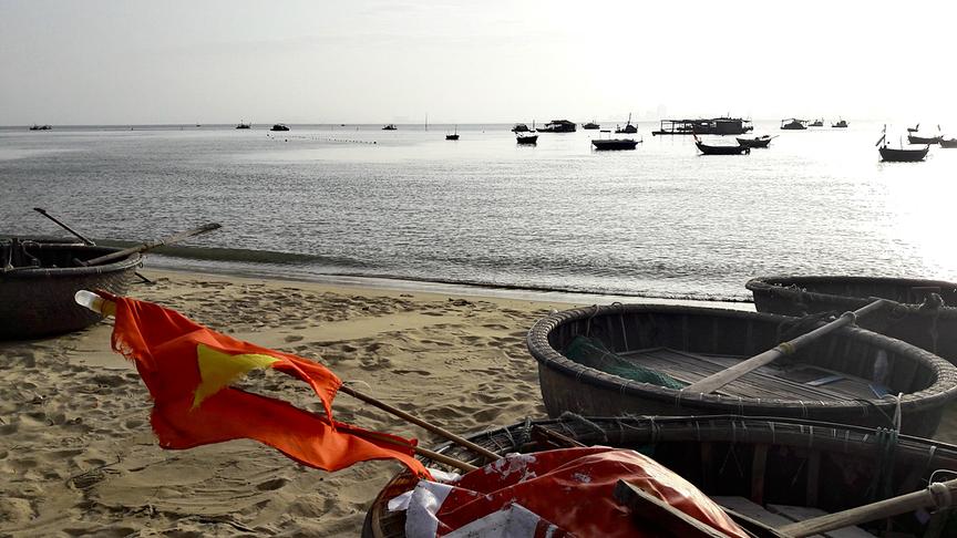 Runde, korbähnlich geflochtene Boote liegen am Sandstrand, während bereits einige andere Boote auf dem Wasser sind.