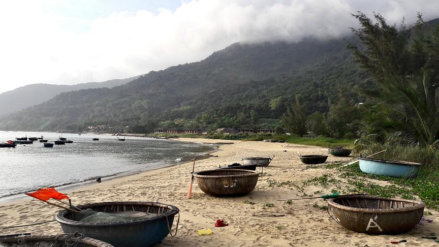 Einem runden Korb ähnlich sehende Boote inklusive Paddel liegen am Sandstrand.