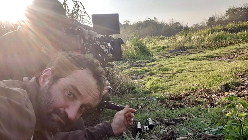 Zwei Kameramänner kommen im Liegen auf einer Grasfläche ihrer Arbeit nach.