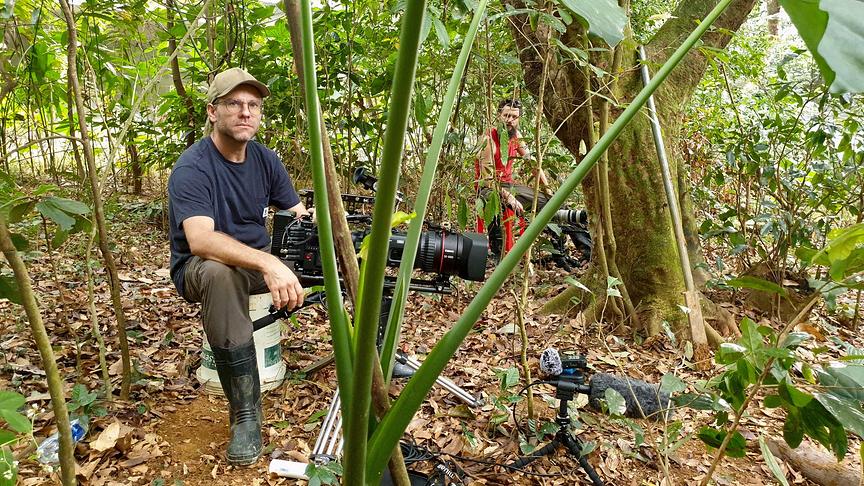 Zwei Kameramänner sitzen mit ihrem Equipment vor sich aufgebaut im Wald.