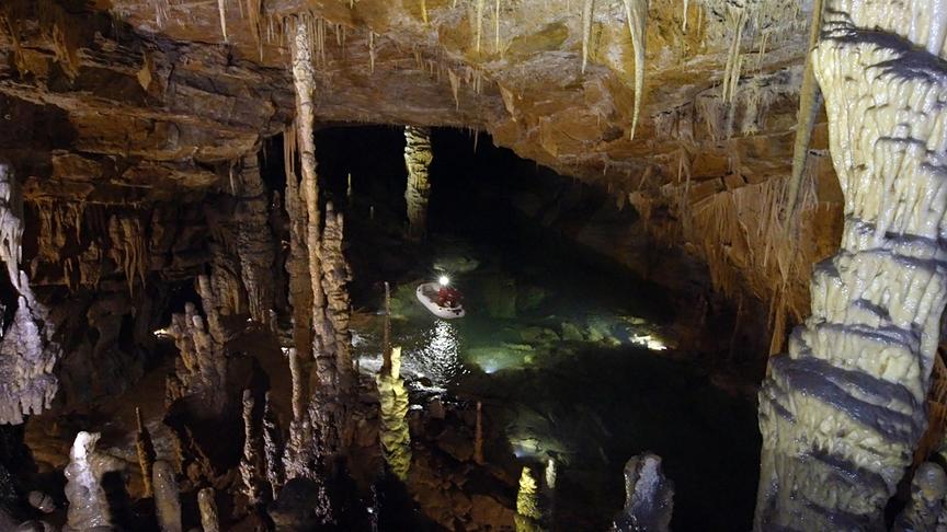 Durch die Höhle mit Tropfsteinformationen und Wasser fährt ein Schlauchboot.