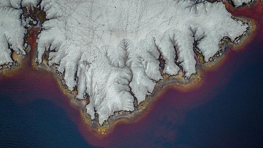 Ein karges Ufer ragt unnatürlich in braun-rötliches Gewässer.