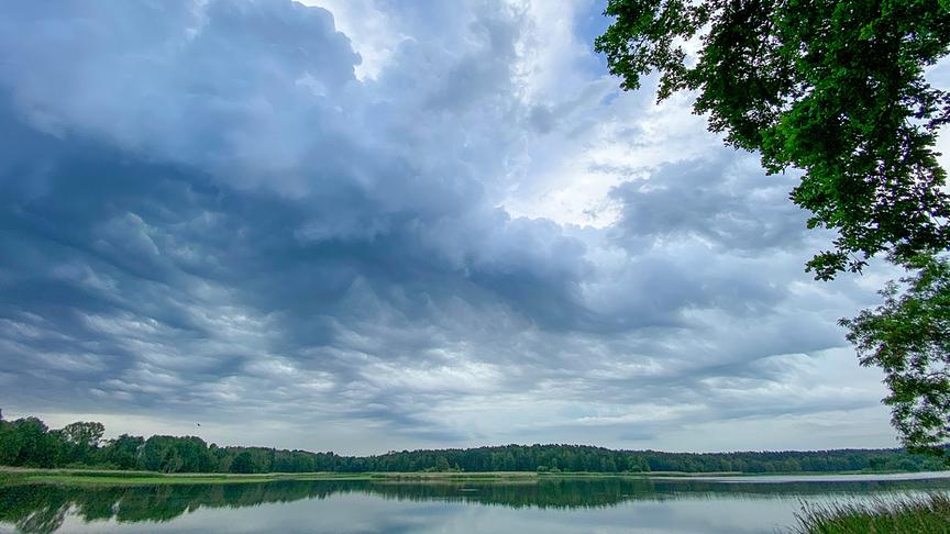 Düstere Wolken über einem See umgeben von Bäumen.