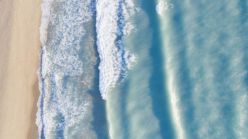 © Foto: ORF/WDR/Plimsoll Productions Ein helltürkises Meer brandet auf einem hellen Sandstrand.