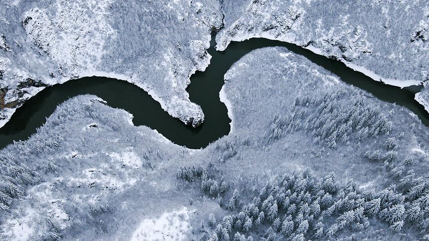 Ein Fluss schlängelt sich durch eine schneebedeckte, winterliche Landschaft.