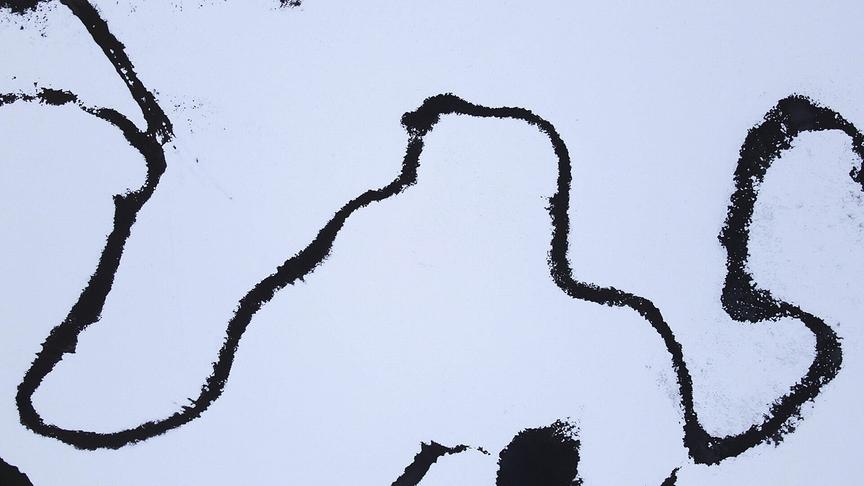 Luftaufnahme eines Flusses, der sich durch eine schneebedeckte Landschaft schlängelt.