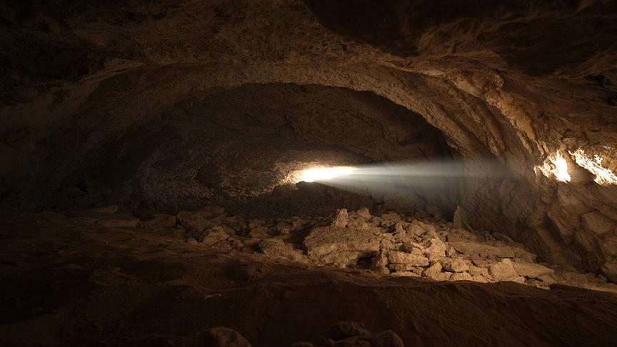 Bild einer dunklen Höhle, ein Lichtstrahl fällt durch einen Spalt im Gestein