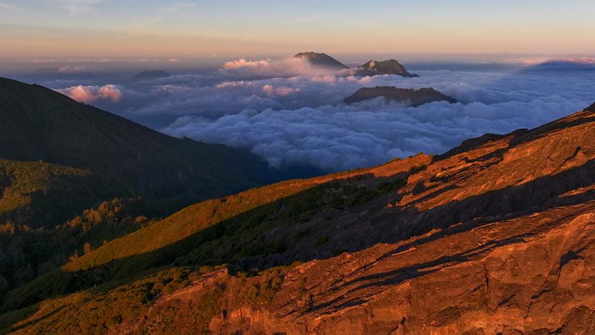 Berge, die aus Nebel- oder Wolkendecke herausragen und von der Sonne in warmes Licht getaucht werden.