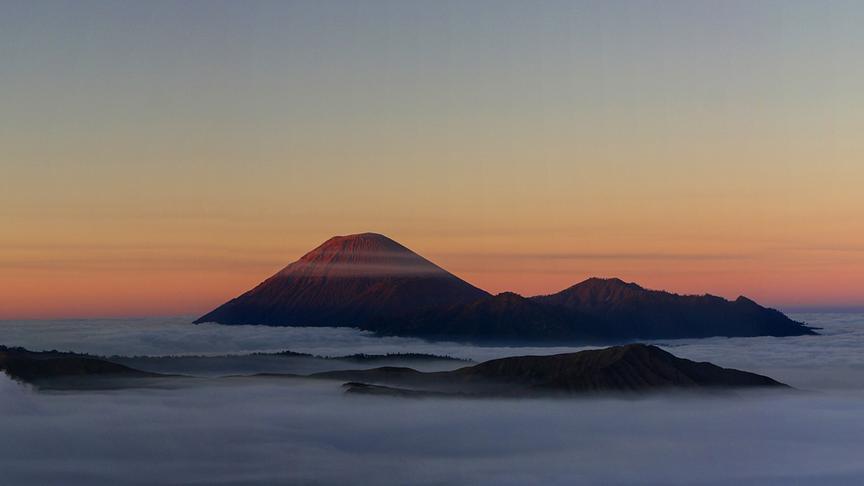 Aus einer Nebeldecke ragende Berggipfel bei Abenddämmerung.