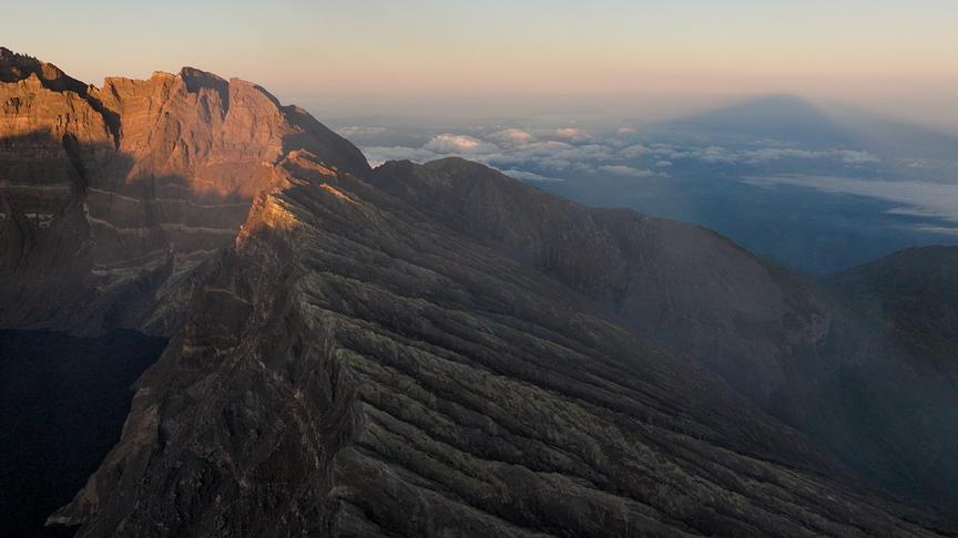 Steil abfallende Felsenwände, im Hintergrund tieferliegende Wolken und der Schatten des Berges.