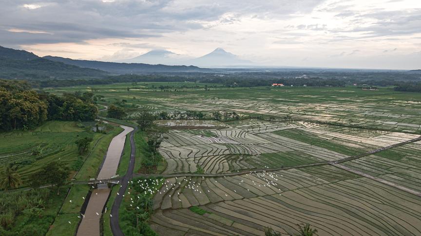 Blick über landwirtschaftlich genutzte Flächen, einen Fluss und Berge.