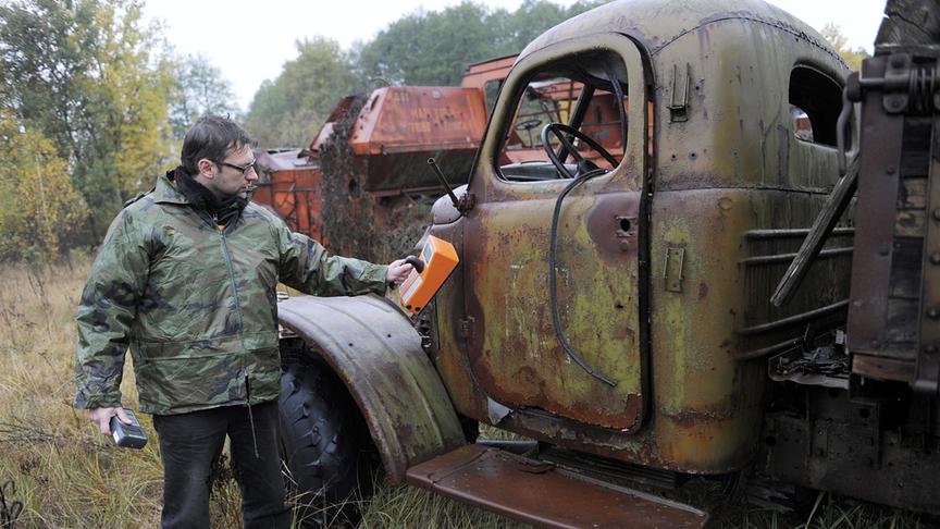 Mann hält Messgerät an einen alten, verrosteten Lastwagen