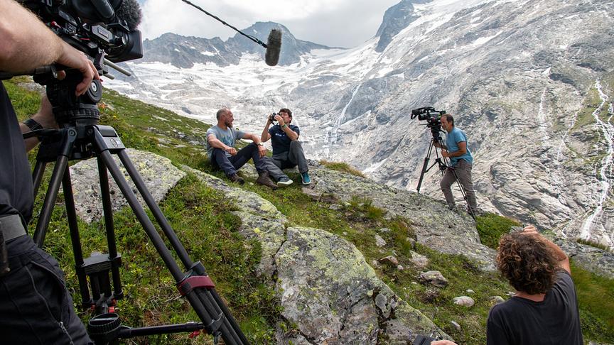 Ein Kamerateam filmt im Hochgebirge eine Dokumentation mit Hermann Maier vor einer alpinen Gletscherkulisse.
