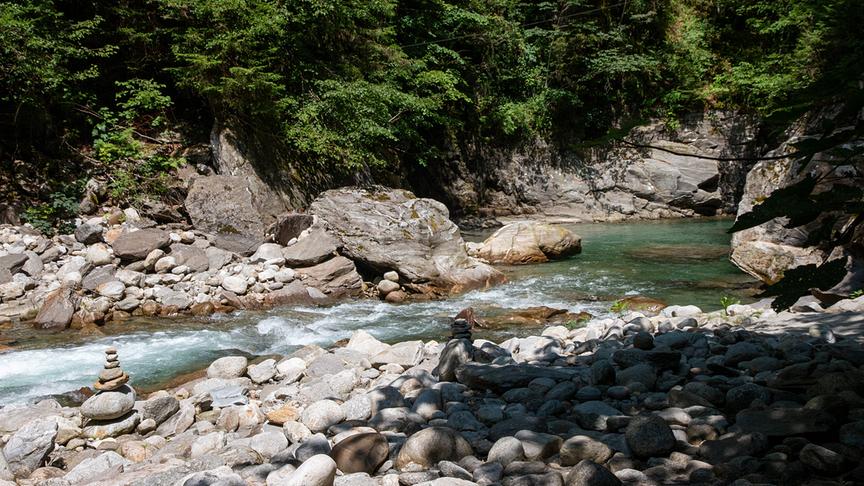 Ein kleiner Bachlauf mit hell-türkisem Wasser fließt zwischen Felsen und Steinen durch den Wald.