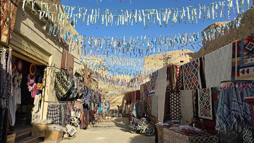 Gasse mit Girlanden und bunten Teppichen und Materialien links und rechts.