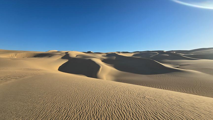 Sanddünen erstrecken sich unter dem blauen Himmel.