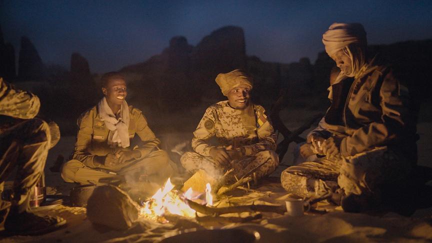 Vier Personen in Camouflage-Kleidung sitzen in der Dunkelheit um ein Lagerfeuer.