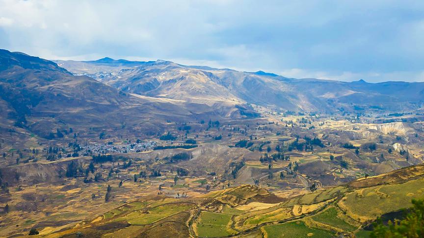 Weites Tal mit klar abgegrenzten Feldern und einer Siedlung im Hintergrund.