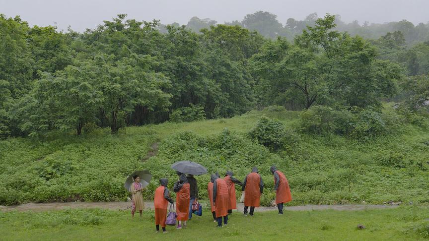 Menschen in Regenkleidung stehen vor einer bewachsenen Böschung und Wald.