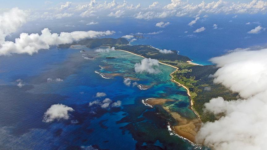 Blick von einem Berg herab auf die längliche Insel, die teils von Wolken verdeckt ist
